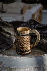 Wooden mug with decorative patterns on a wooden surface, with a blurred background of a cozy room.